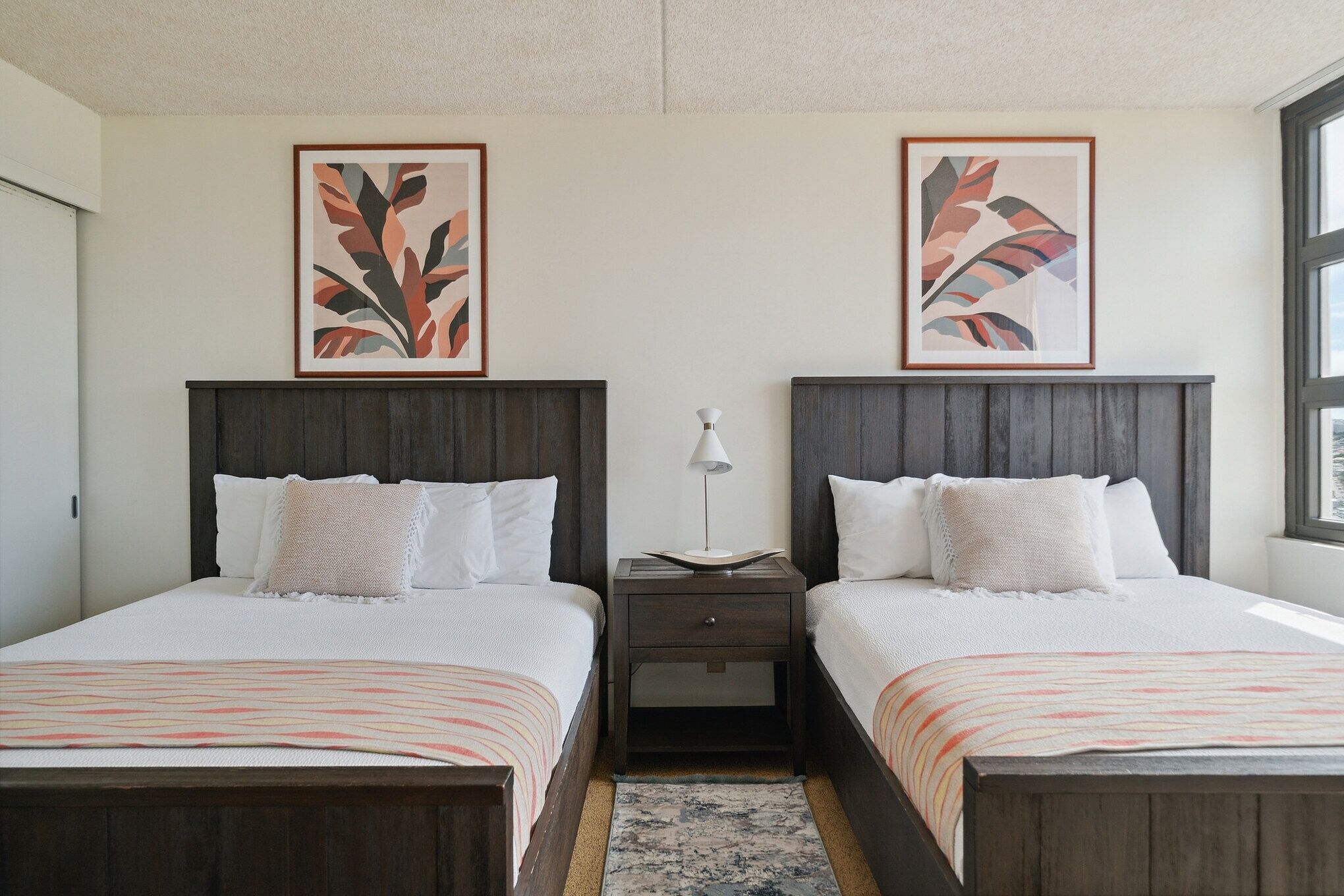 A double room with two beds, a nightstand between them, and a window on the right.