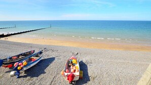 Ein Kiesstrand mit zwei kleinen Booten, eines mit einer roten Plane und das andere mit einer blauen Plane, und einer anlegenden Mole.