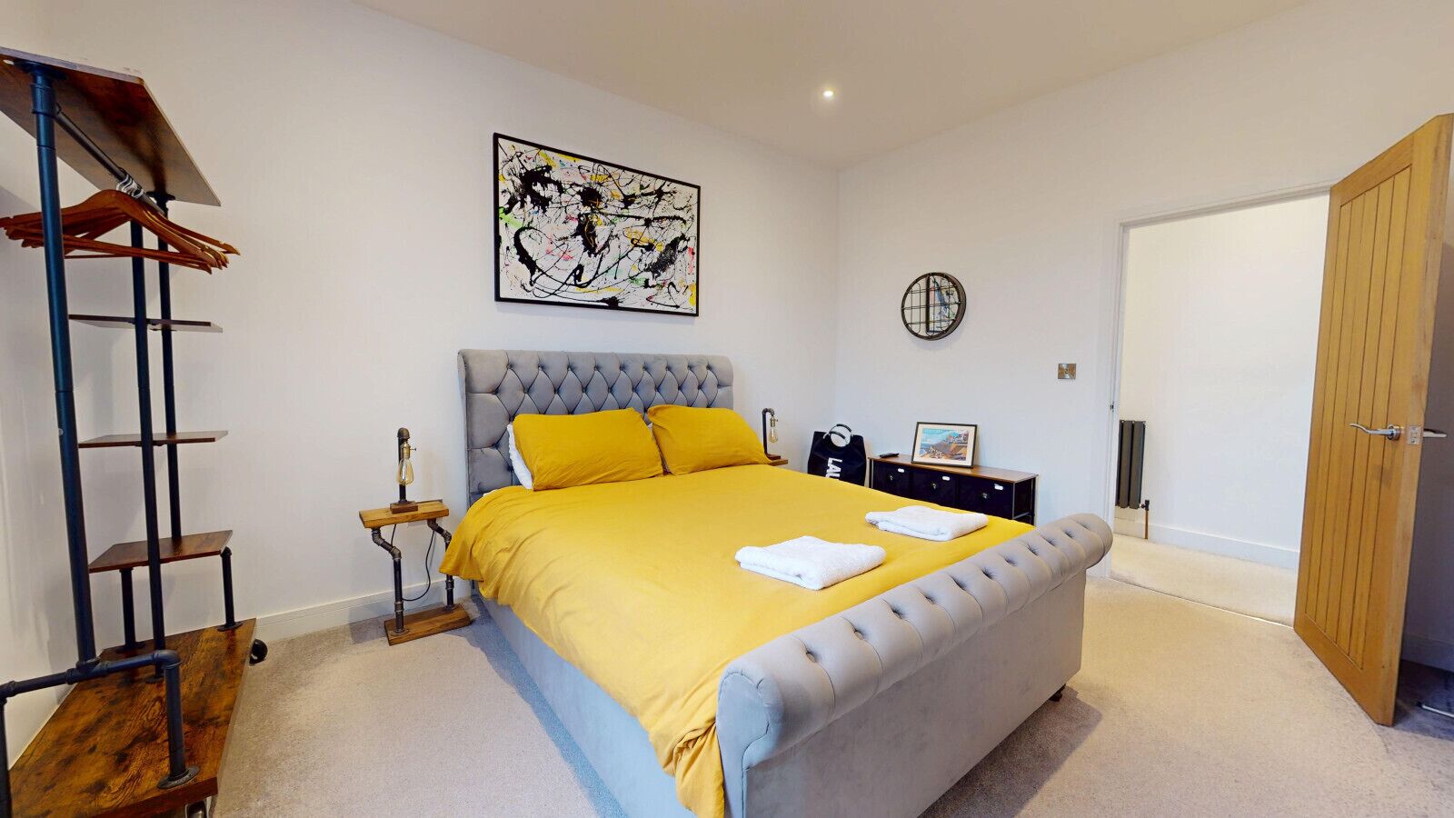A bedroom with a bed, a nightstand, a lamp, a wall clock, and a door.