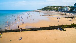 Ein Strand mit einer Steinmauer, Menschen und Gebäuden im Hintergrund.