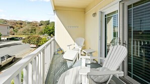 A balcony with white Adirondack chairs and a small table, overlooking a parking area and a hilly landscape. - Sunny Rio Del Mar Beach Townhome – Relax, Unwind & Enjoy the Coast (Aptos)