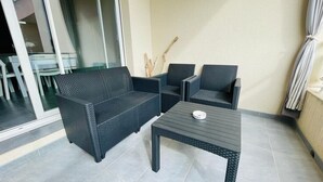 Ein Balkon mit einer dunklen Rattan-Couch, zwei passenden Sesseln und einem kleinen Tisch mit einer Schale.