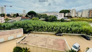 Ein Parkplatz mit mehreren Autos, umgeben von Grünflächen und Gebäuden im Hintergrund.