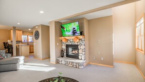 A living room with a stone fireplace, a flat-screen TV mounted above it, and a dining area in the background.