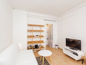 A modern living room with a white sofa, a small round table, a TV on a white stand, and a wooden shelf unit against the wall. - Charming studio near Paris with balcony (Vincennes)