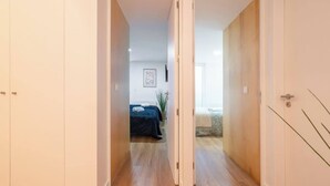 Un couloir au plancher de bois menant à une chambre à coucher équipée d’un lit et d’une table de chevet.