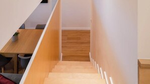 Un intérieur moderne avec un escalier en bois, un petit coin salon et une porte visible en haut de l’escalier.