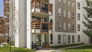 Un edificio residencial de varios pisos con balcones, un acceso cubierto y un pequeño espacio de esparcimiento al aire libre.