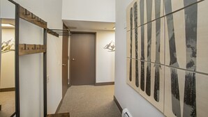 Un pasillo con una escalera de madera, una puerta y un muro con baldosas de diseño vertical.