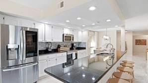 A modern kitchen with stainless steel appliances, white cabinetry, and a central island with stools.