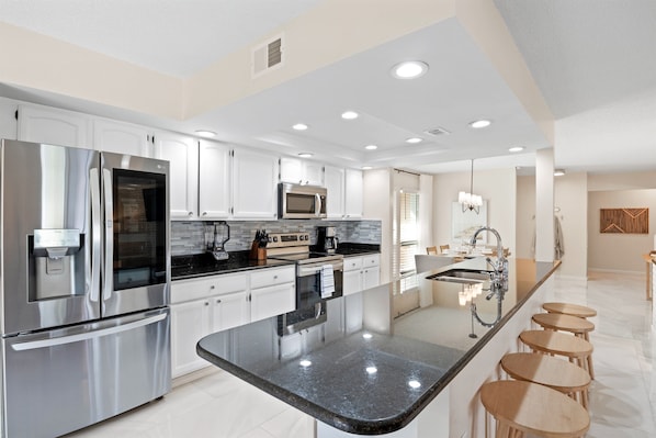 A modern kitchen with stainless steel appliances, a central island with bar stools, and recessed ceiling lighting.
