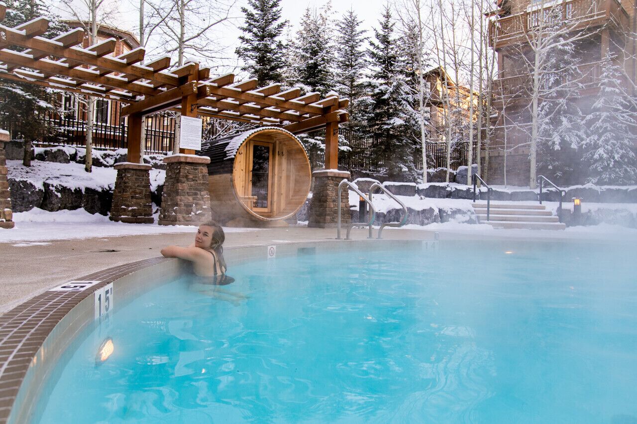 Ein Whirlpool mit einer hölzernen Pergola und einer Holzbottstruktur in verschneiter Landschaft.