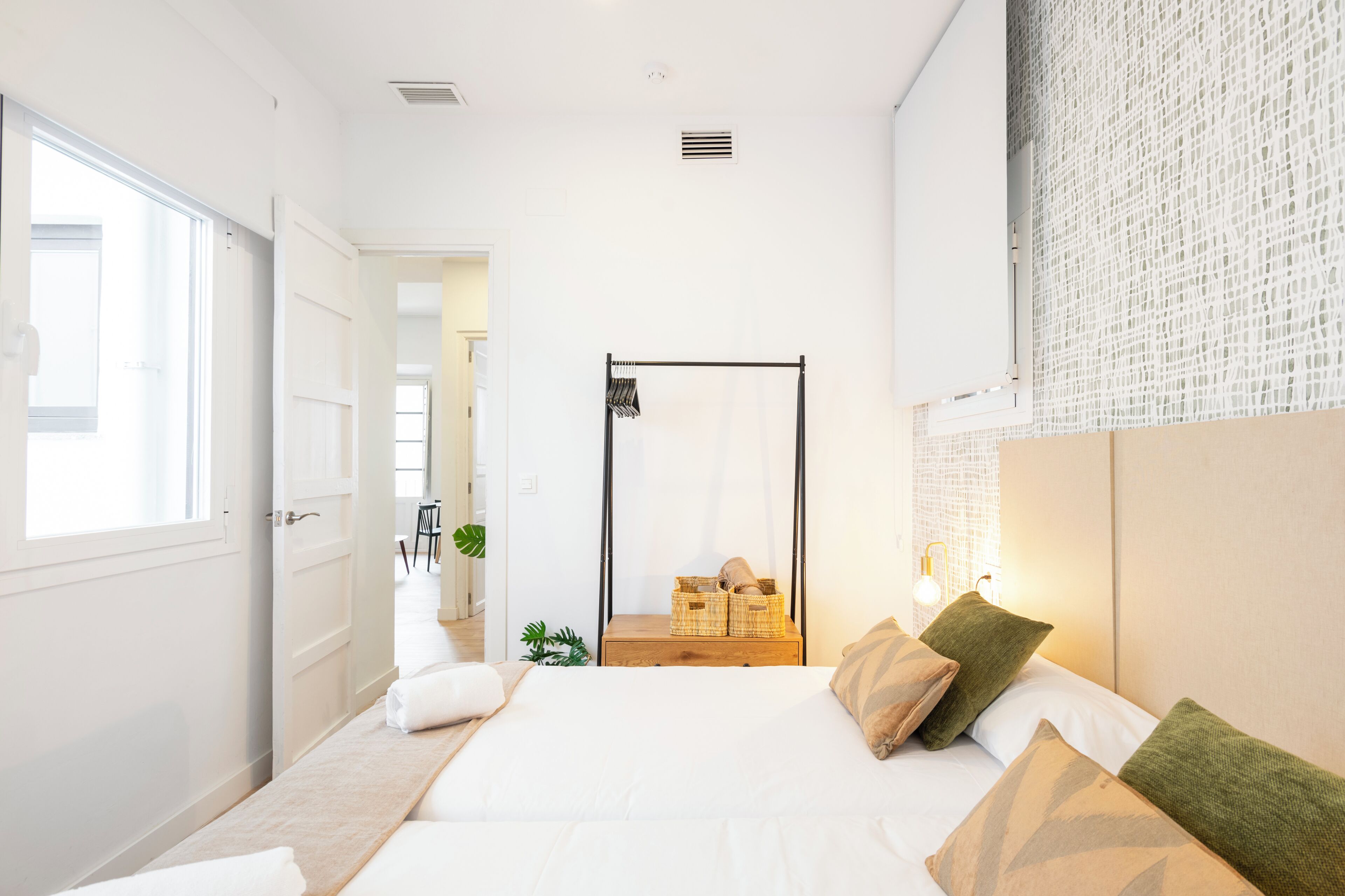 A modern bedroom with a large bed, a bedside table, a mirror, and a window.