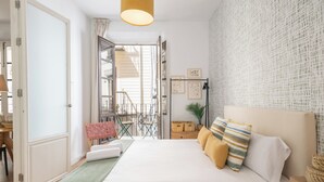 A bedroom with a bed, a green throw, a wooden nightstand, and a view of the outside balcony. - Apartamentos Luna Suites Palacio Dorita (Granada)