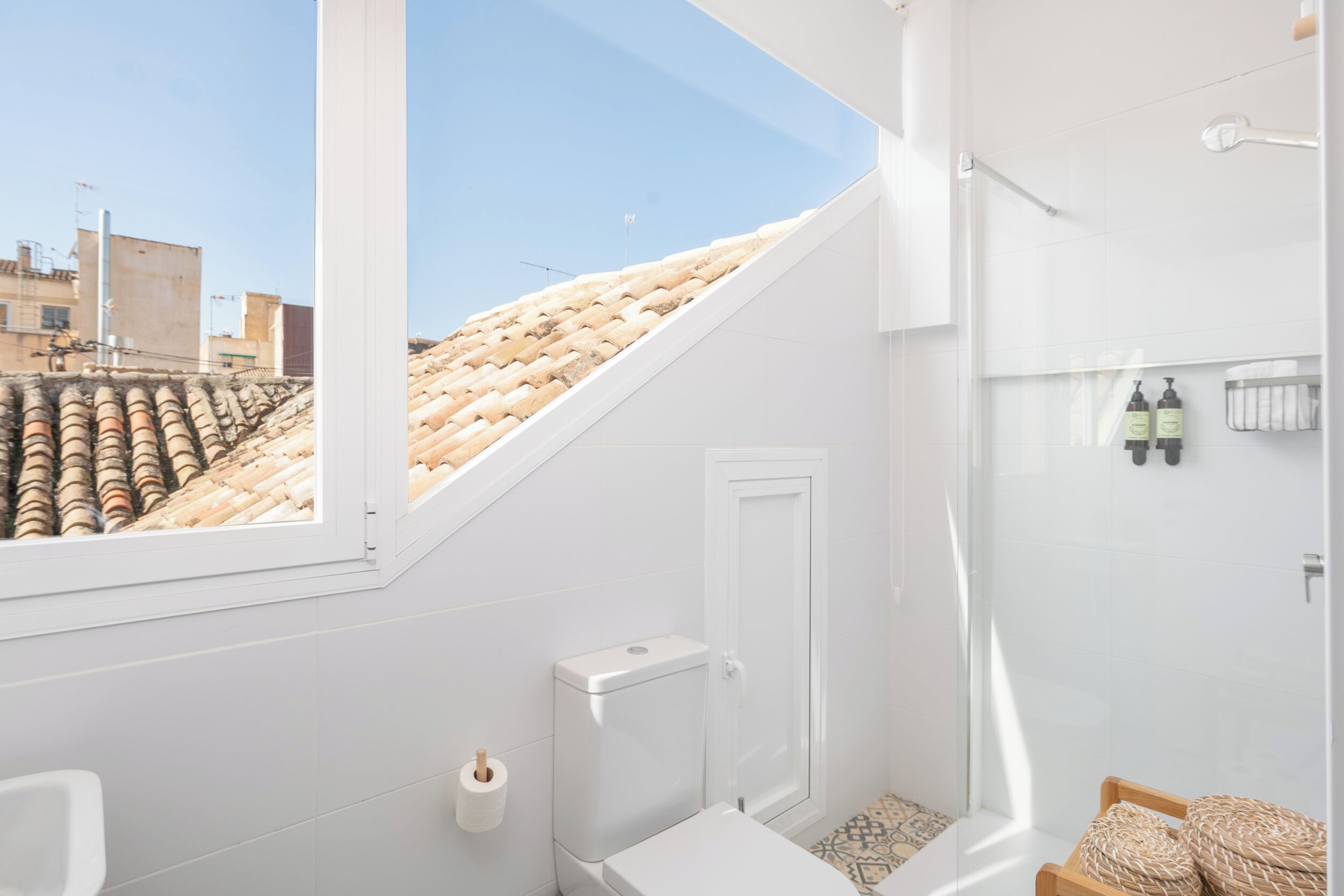 A modern bathroom with a skylight, a toilet, a shower, and a small shelf with toiletries.