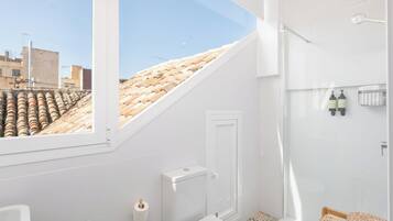 A modern bathroom with a skylight, a toilet, a shower, and a small shelf with toiletries.