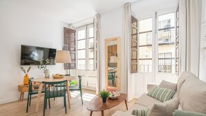 A modern living room with a sofa, a coffee table, a TV, and a dining area with a table and chairs. - Apartamentos Luna Suites Palacio Dorita (Granada)
