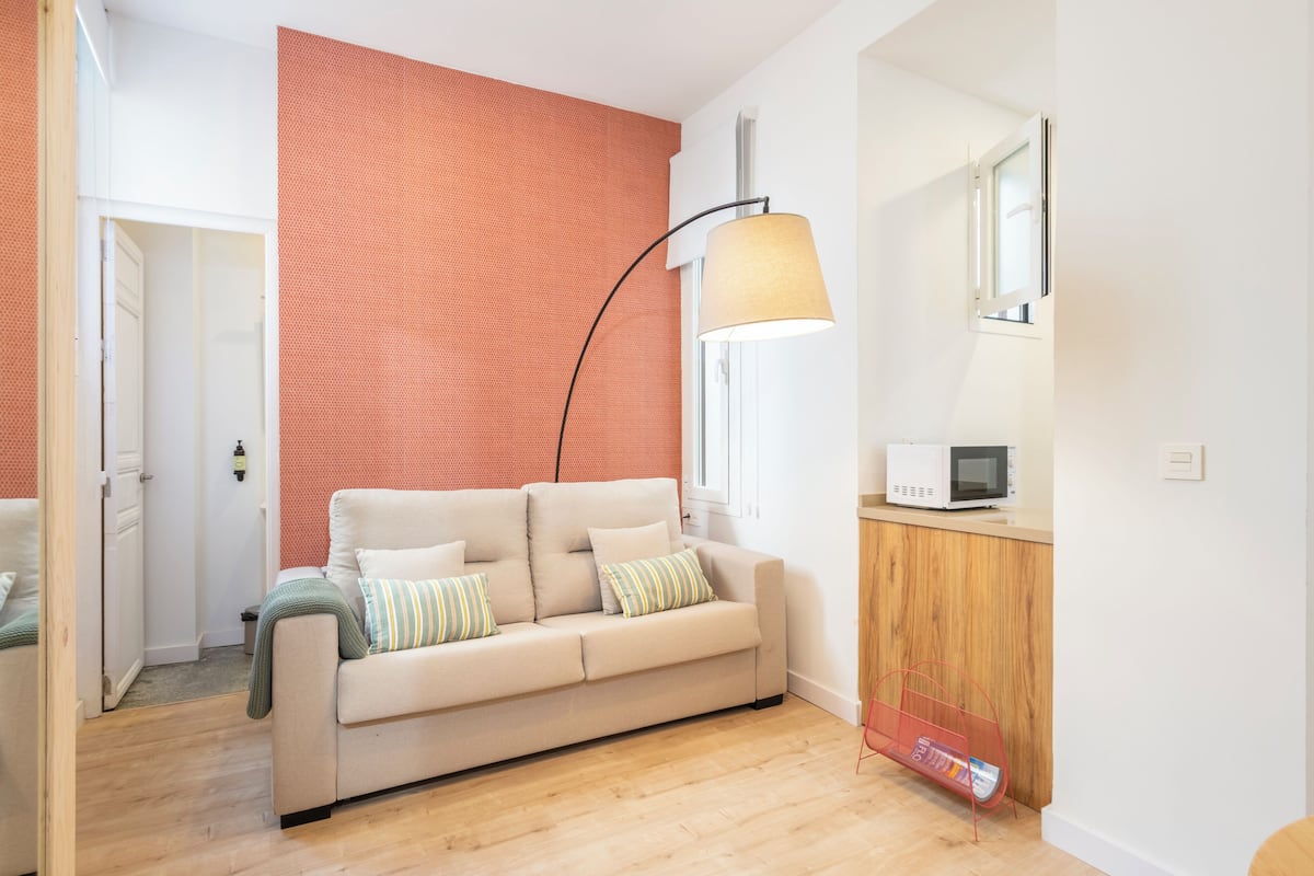 Un salon moderne avec un canapé beige, un mur rouge à texture, un lampadaire, un four à micro-ondes et un meuble en bois.
