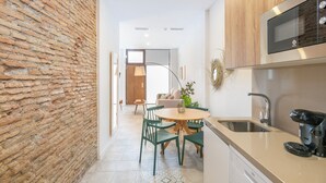 A modern kitchen with a brick wall, wooden cabinets, a built-in microwave, and a dining area with chairs and a table. - Apartamentos Luna Suites Palacio Dorita (Granada)
