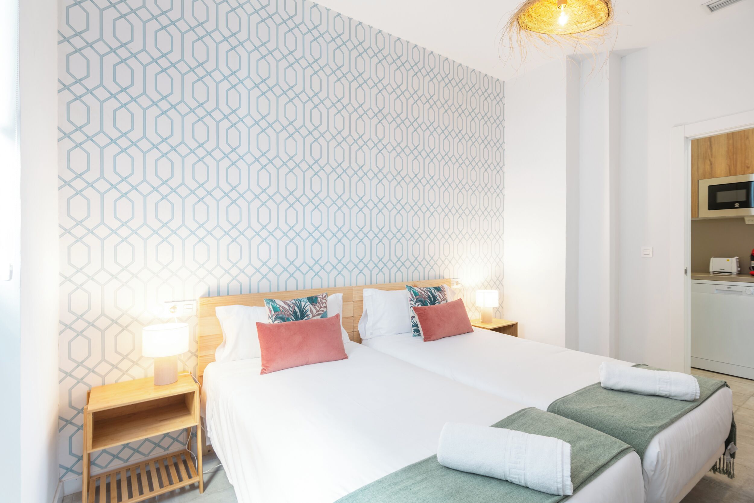 Una cama doble con dos almohadas, una mesita de noche con una lámpara y una pared con diseño.