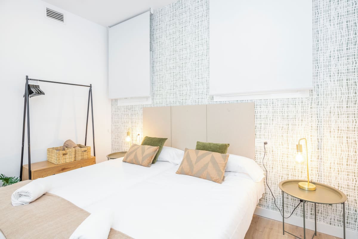 Une chambre d’hôtel moderne avec un grand lit, deux oreillers, une table de chevet avec une lampe et un mur orné d’un motif en mosaïque.