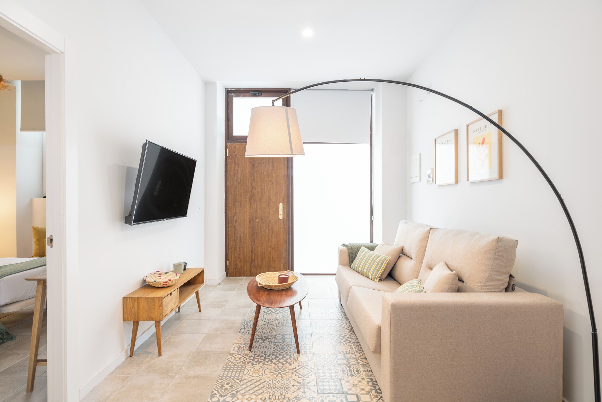 Un salón moderno con un sofá, un televisor instalado en la pared, una mesita de madera y una alfombra estampada.
