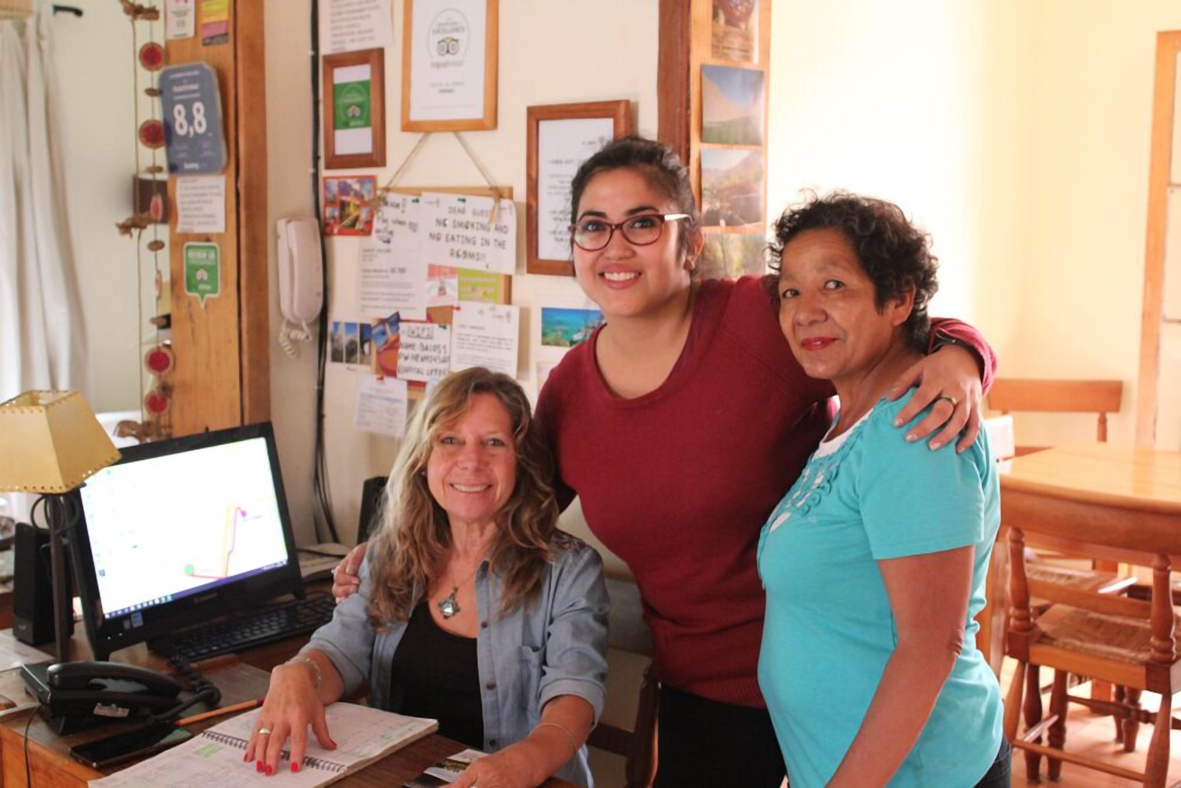 Tres personas en un entorno de oficina, con una computadora, papeles y una pizarra con varios avisos.