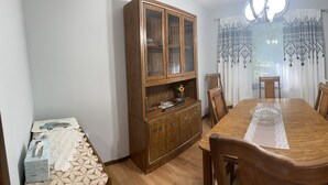 Un comedor con una mesa de madera, sillas, un armario y una cocina visible a través de una puerta abierta.
