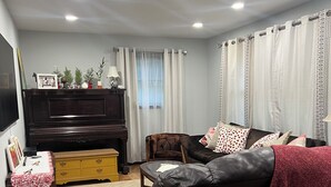 Una sala de estar con un sofá marrón oscuro, un mueble amarillo, una mesa de centro de madera, un televisor y un piano.