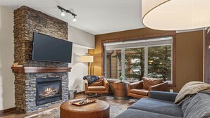 Een moderne woonkamer met een stenen open haard, lederen meubels en een groot raam met uitzicht op bomen.