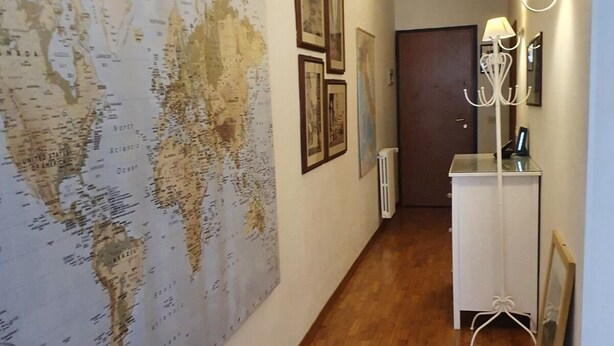 A hallway with a large world map on the left wall, framed pictures above a white radiator, and a white cabinet with a lamp on the right. - In Florence, in the heart of dowtown (Firenze)