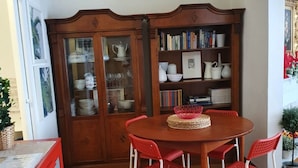 A dining area with a wooden table and red chairs, a wooden cabinet with glass doors, and a bookshelf filled with books and decorative items. - In Florence, in the heart of dowtown (Firenze)