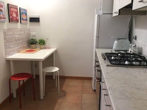 A compact kitchen with a gas stove, a white countertop, a small dining table with two stools, and a tiled backsplash.