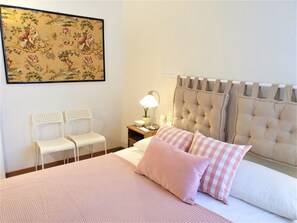 A bedroom with a bed, two chairs, a nightstand with a lamp, and a headboard.