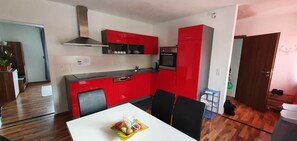 A compact kitchen with red cabinets, a stainless steel range hood, and a built-in oven.