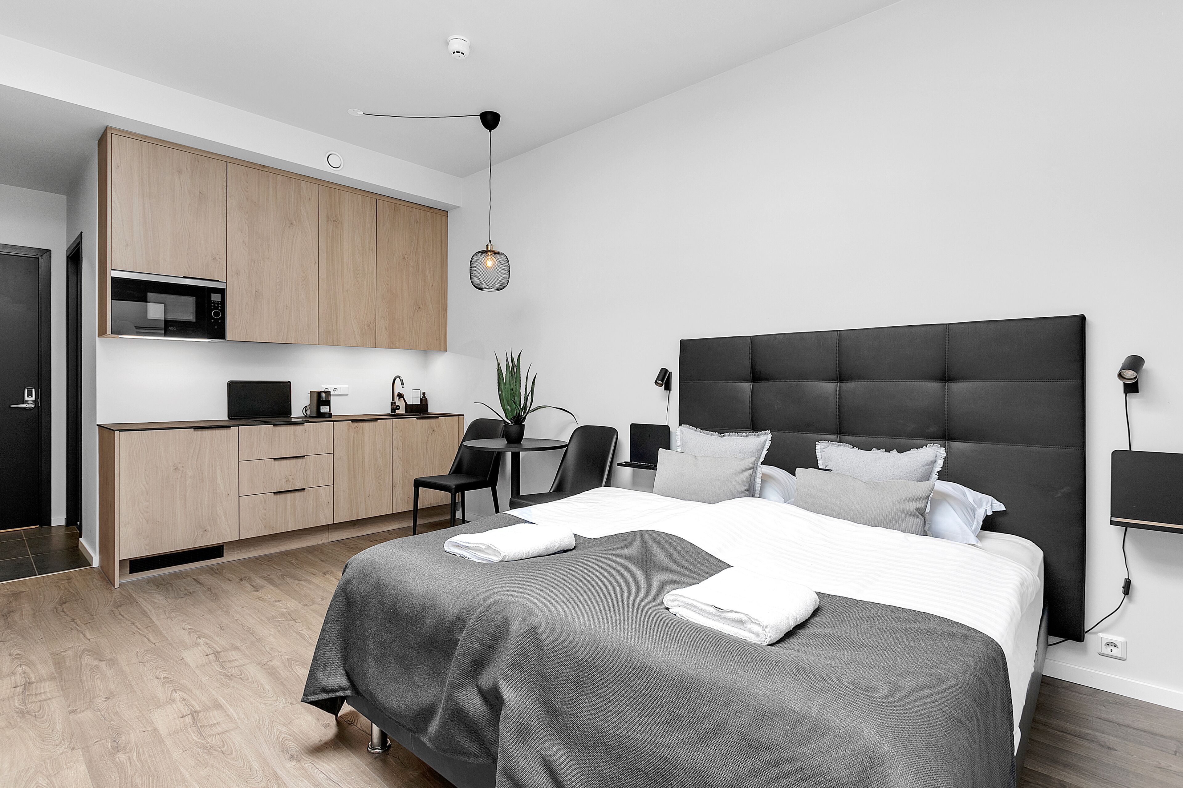 A modern bedroom with a large bed, a desk, and a kitchenette.