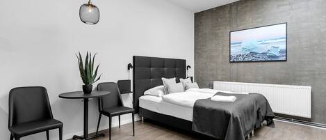 A modern bedroom with a bed, two chairs, a small table, a potted plant, and a large window.