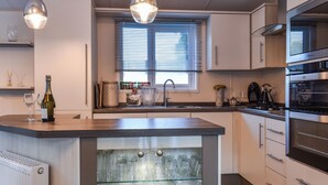 Une cuisine moderne dotée d’un îlot central, d’appareils électroménagers en acier inoxydable et d’un meuble à vin avec une porte en verre.