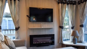 Un salon doté d’un téléviseur à écran plat fixé au mur, d’une cheminée en dessous et d’un canapé agrémenté de coussins à motifs.