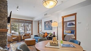 Ein modernes Wohnzimmer mit einem runden Holztisch, Ledersofas und einem großen Fenster mit Blick auf eine verschneite Straße.