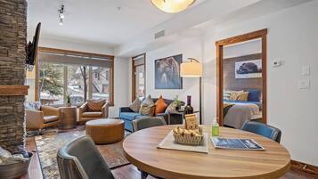 A modern living room with a round wooden table, leather sofas, and a large window with a view of a snowy street.