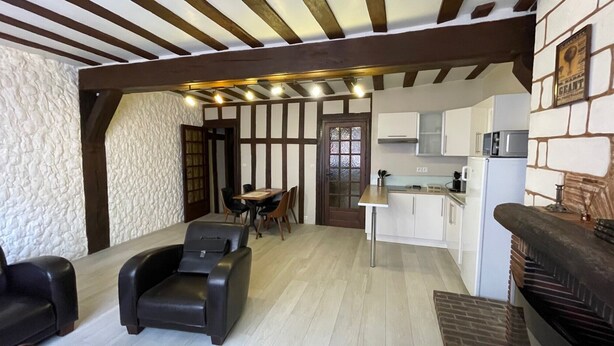 A cozy room with a dining table, chairs, a massage chair, a kitchen with cabinets and appliances, and a stone wall.
