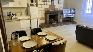 A modern kitchen with white cabinets, a microwave, and a built-in oven. There is a dining area with a wooden table set for four, and a television in the background.