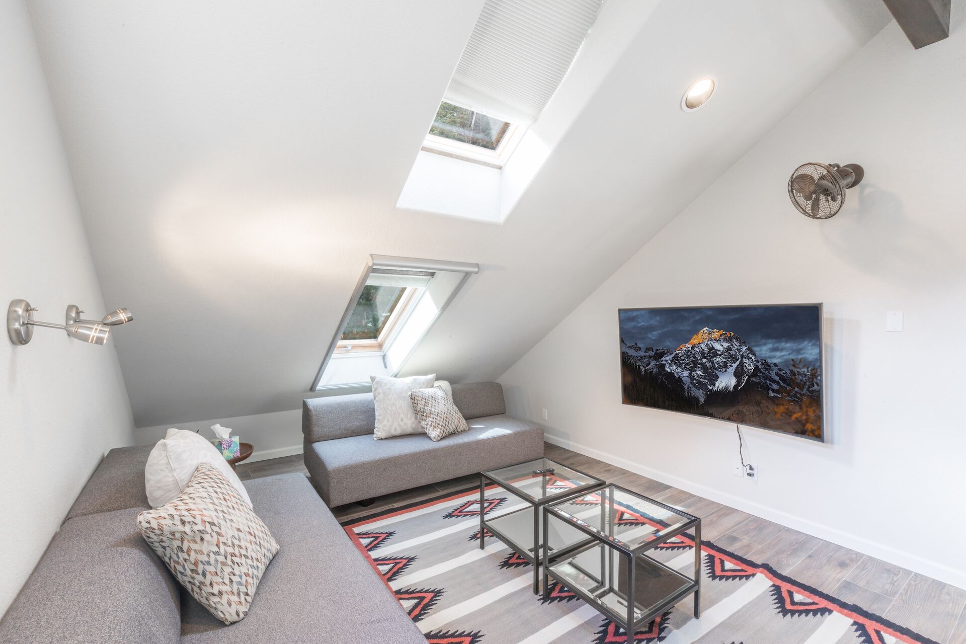 A modern loft bedroom with a sloped ceiling, skylight, and a large mountain painting.