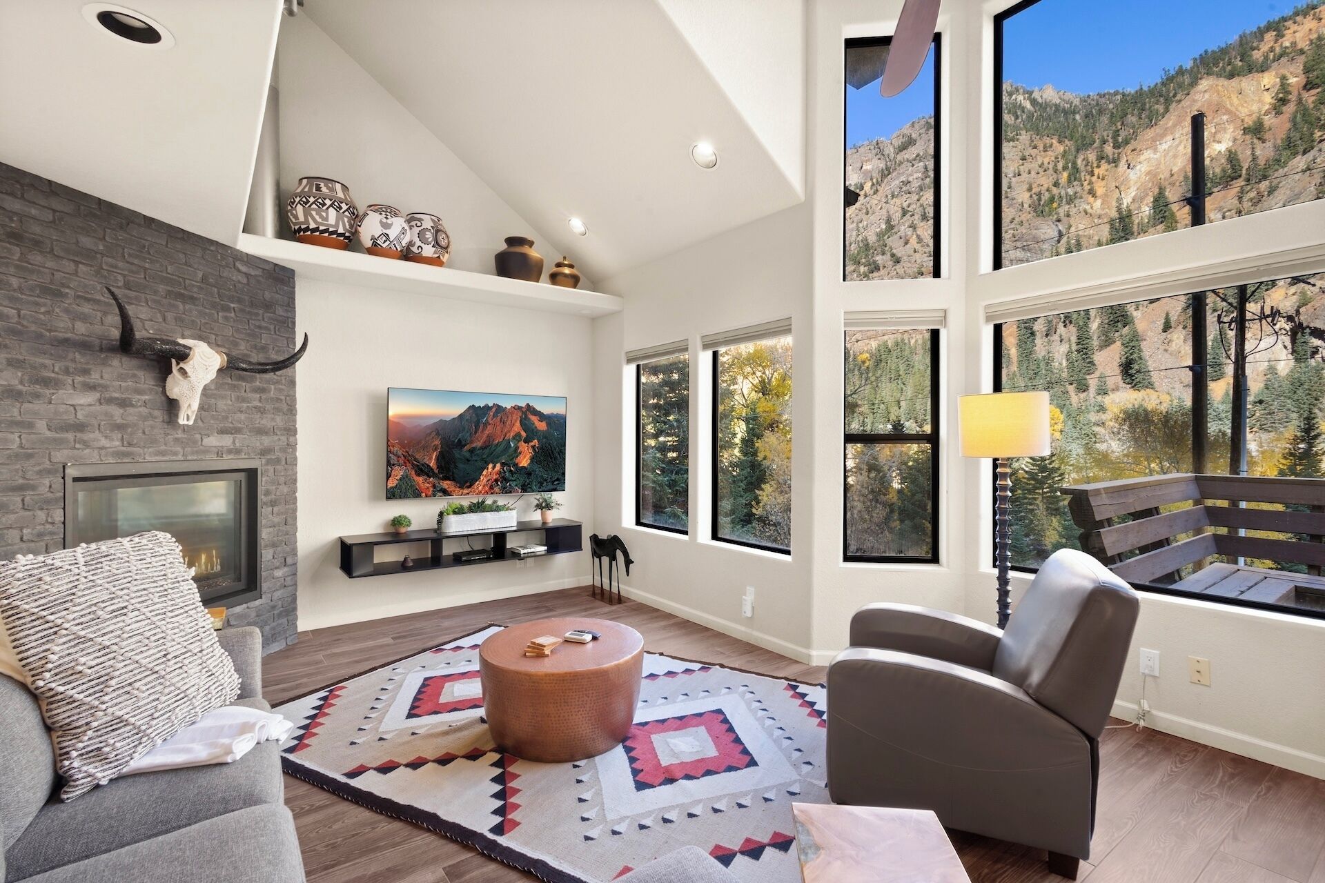 A modern living room with a fireplace, large windows, and a mountain view.