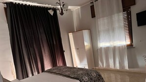 A bedroom with a bed, a wardrobe, a mirror, and a window with curtains. - Hotel Vistamare (Pozzuoli)