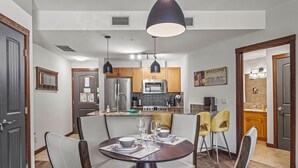 A modern kitchen with stainless steel appliances, a dining area with a round table and chairs, and a "Welcome" sign on the wall. - 180° Mountain Views | Two Hot Tubs | New Design (Canmore)