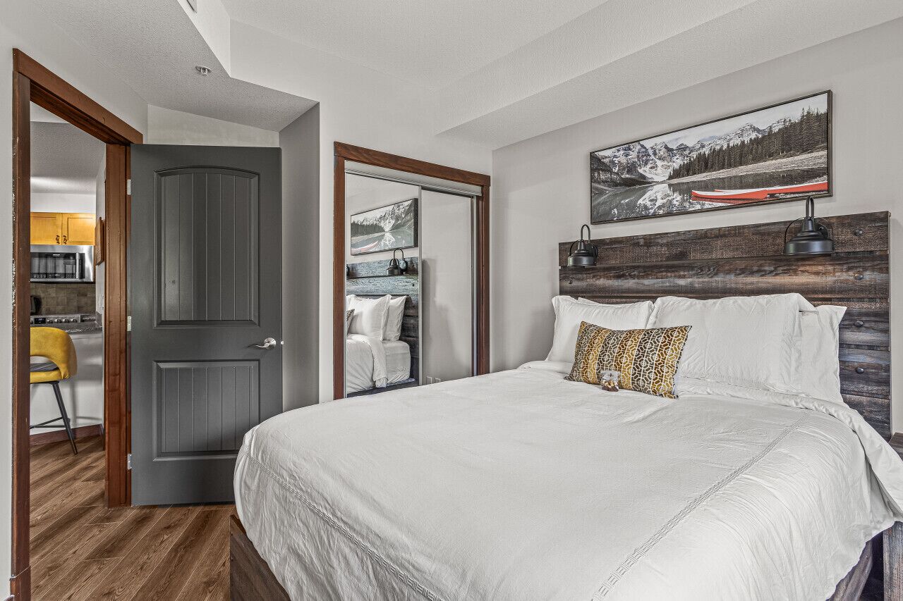 A bedroom with a large bed, a wooden headboard, a mirror, and a painting of a mountain landscape.