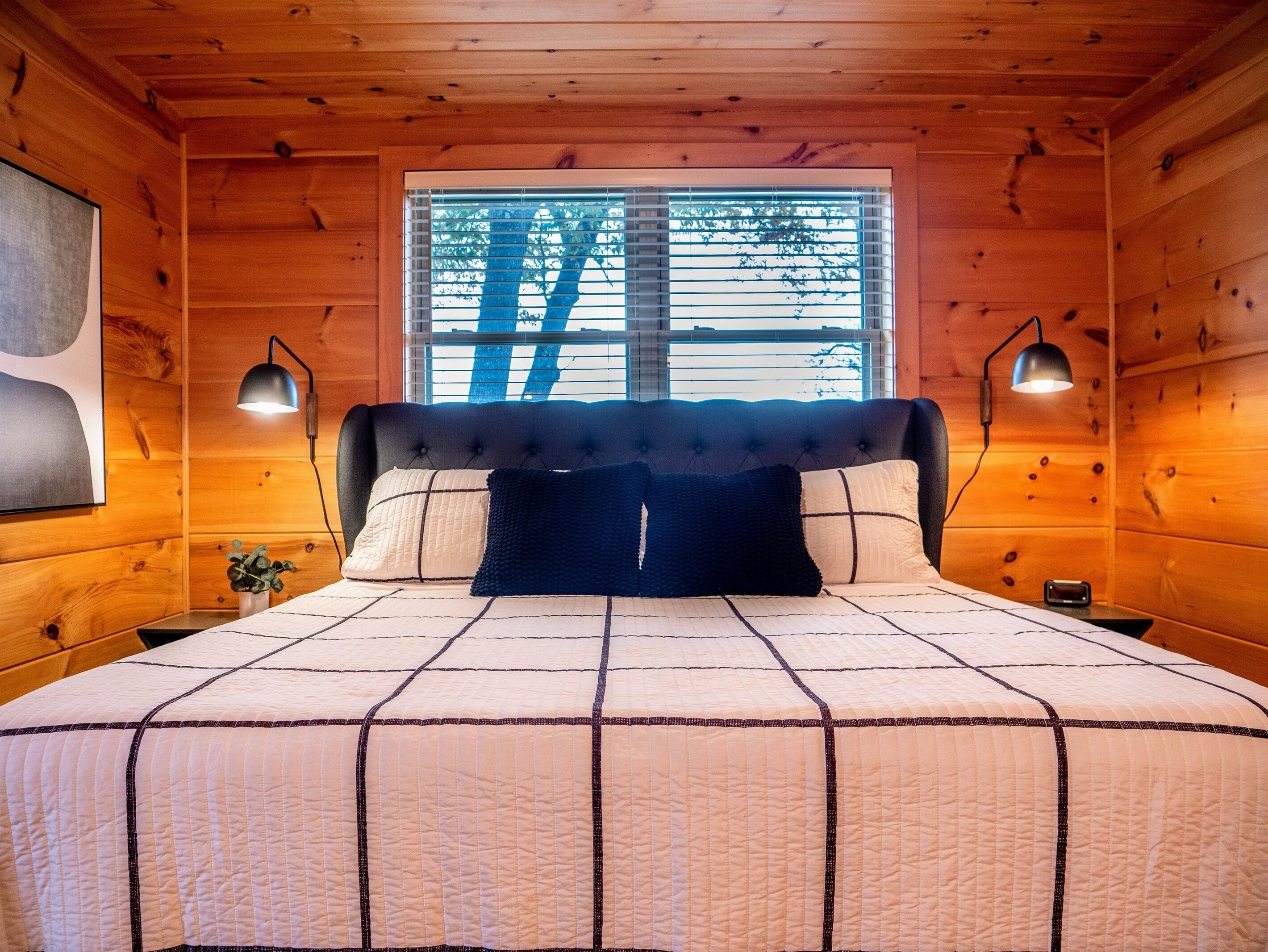 Une chambre à coucher dans un chalet en bois, avec un grand lit, deux lampes de chevet et une fenêtre avec des stores.
