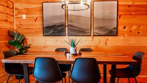 Une pièce aux murs lambrissés, avec une longue table et des chaises noires, une plante en pot et deux tableaux encadrés accrochés au mur.